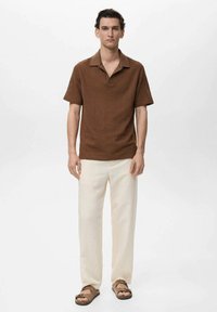 Brown textured short-sleeve polo shirt, cream trousers, brown sandals. Simple collar and relaxed fit. Plain background, no additional details.