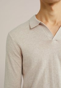 Pulover tricotat de un bej deschis, cu decolteu în V și textură moale. Are un guler scurt și mâneci lungi, fiind proiectat pentru o potrivire confortabilă.