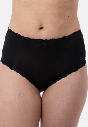 Frau in schwarzer Baumwoll-Hochbundunterwäsche mit Spitzenbesatz und kleinem Frontbogen, die ihren Mittelbauch und die Oberschenkel auf einem weißen Hintergrund zeigt.