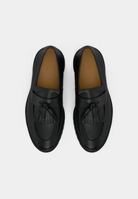 Zwarte leren instappers met een gladde afwerking, voorzien van een kwastjesontwerp en gestikte accenten langs de zool. Plat, rond teengedeelte.