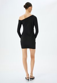 Robe noire à manches longues avec un décolleté asymétrique, une silhouette ajustée et une longueur au-dessus du genou. Tissu lisse et extensible avec un minimalisme dans les détails.
