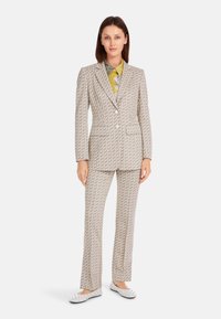 Gray patterned suit with a fitted blazer and straight-leg trousers, paired with a multicolored collared shirt and white flats.