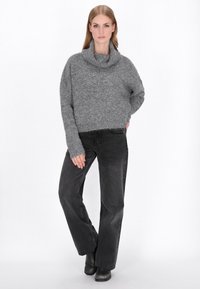 Grau gestrickter Pullover mit einem Schalkragen, kombiniert mit schwarzen hoch taillierten Jeans. Die Textur wirkt weich und fusselig. Schwarze Knöchelstiefel runden den Look ab.