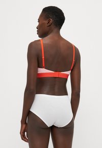 Soutien-gorge avec un blocage de couleurs rose et orange, bretelles réglables orange et fermeture à crochets. Assorti à une culotte taille haute blanche.
