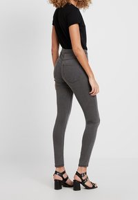 Vaqueros gris de talle alto con corte ajustado, con bolsillos traseros, complementados con sandalias negras de tacón bloque y una blusa negra ajustada.