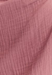 Lahka, nagubana tkanina v nežni rožnati barvi, z mehko teksturo in subtilnimi, neenakomernimi črtami. Idealna za raznolike namene.