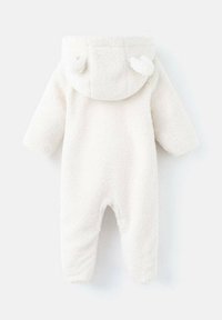 Mono de nieve para bebés de tela de felpa blanca con capucha, que presenta pequeñas orejas redondeadas, mangas largas y diseño de pies abiertos. Textura suave con un ajuste acogedor.