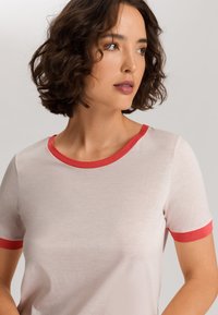 Camiseta rosa claro con escote redondo, de mangas cortas y con ribetes rojos en el cuello y las mangas; textura suave y lisa.