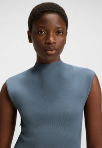 Blue, fitted top made of textured fabric with a high neckline and sleeveless design. Features a subtle side seam detail.