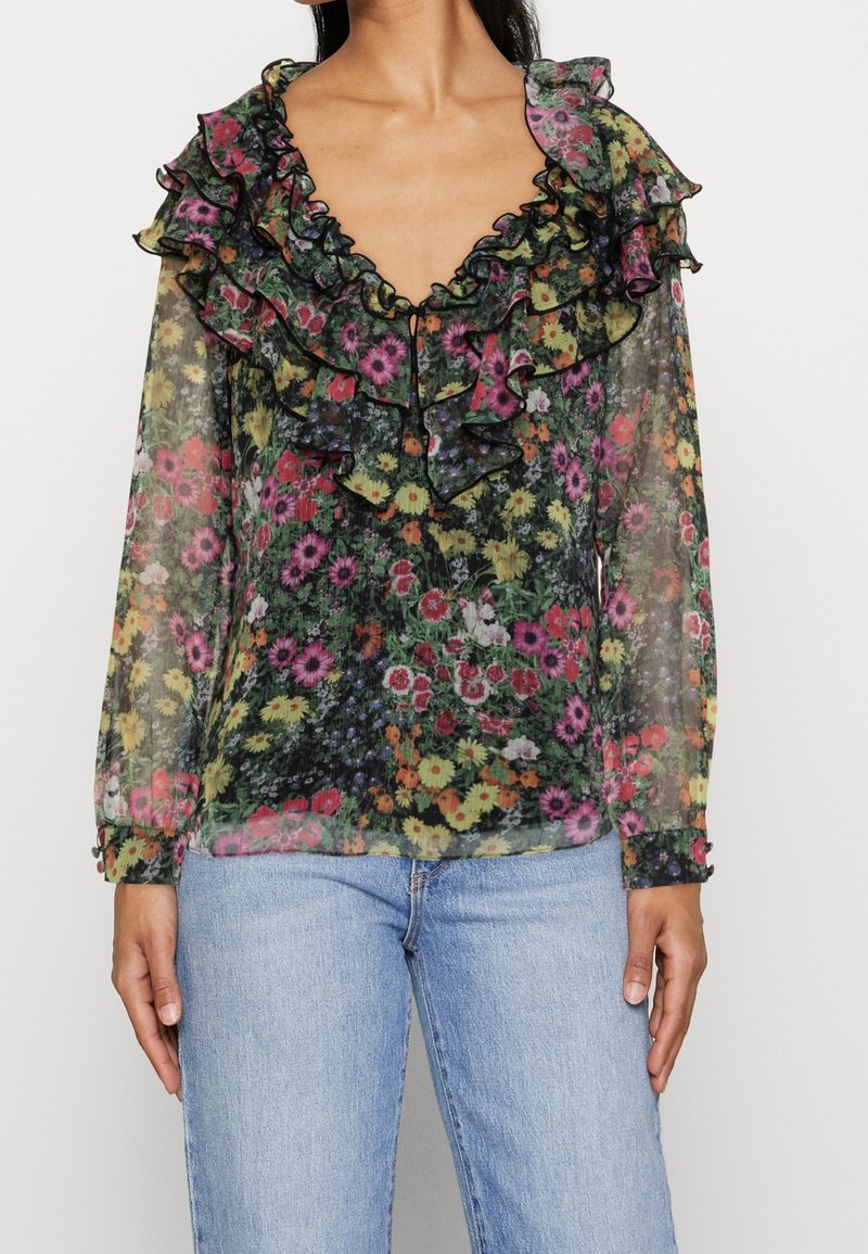 Blouse noire transparente avec un motif floral vibrant, dotée d'un col et de poignets volantés avec une bordure contrastante ; manches longues et coupe décontractée.