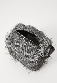 Sac en noir et blanc à motif chevrons texturé avec des bords effilochés, doté d'une fermeture éclair argentée et d'une doublure noire. Ouverture zippée sur le dessus.