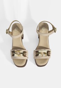 Beige Wildleder-Sandalen mit einem Knöchelriemen, breitem Vorderband mit einer weißen rechteckigen Schnalle und goldfarbenen Beschlägen, flache Sohle.
