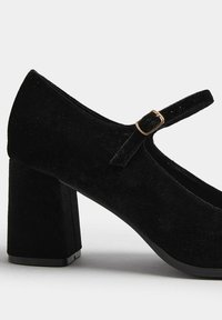 Scarpa Mary Jane in velluto nero con punta rotonda, tacco spesso a blocco e una cintura fissata da una fibbia in tonalità oro. Texture liscia e colore solido.