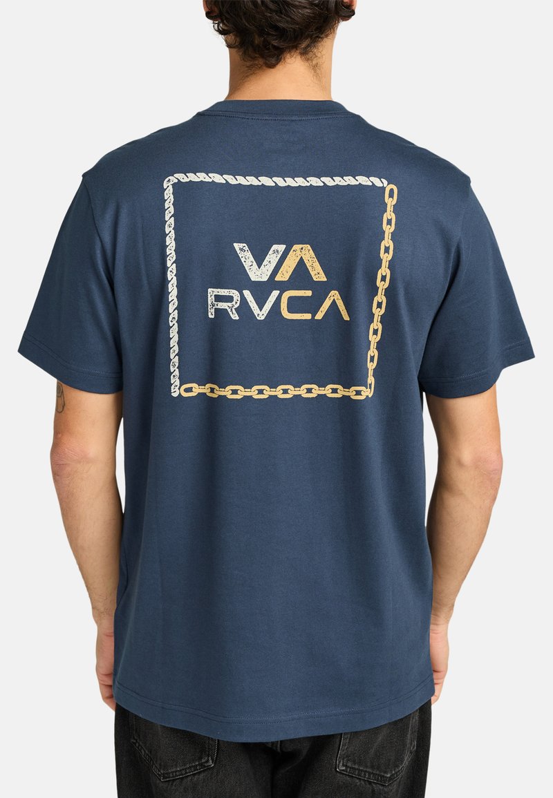 Camiseta de algodón azul marina con un diseño gráfico de cadena y cuerda dorada, con el logo 'VA RVCA' centrado en la parte posterior. Manga corta, ajuste relajado.