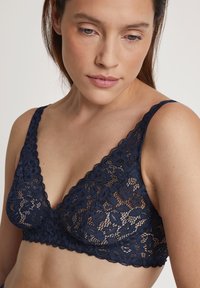 Marinblå spets-bh med blommönster, djup V-ringning och breda remmar. Mjuk textur utan vaddering för komfort.
