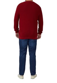 Roter gerippter Pullover mit rundem Ausschnitt, langen Ärmeln und lockerem Schnitt, kombiniert mit blauen Denim-Jeans und hellfarbigen Sneakers.