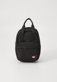 Sac à dos en tissu noir avec deux poignées supérieures, poche zippée frontale, et un patch logo en rouge, blanc et bleu sur le bas avant.