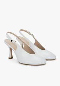 Witte slingback hakken hebben een glanzende lakleren afwerking, een puntige neus en een slanke stilettohak met een gespsluiting op de band.