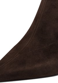 Gros plan sur une botte cheville en daim brun foncé avec des coutures visibles le long de son côté courbé et une semelle lisse.