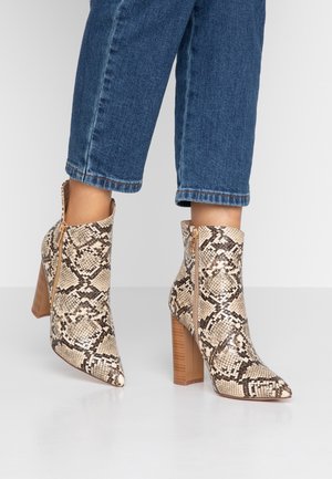 Bottines à imprimé serpent avec un bout pointu, teintes beige et marron, comportant une fermeture éclair sur le côté et un talon empilé. Détail de surface texturée visible.