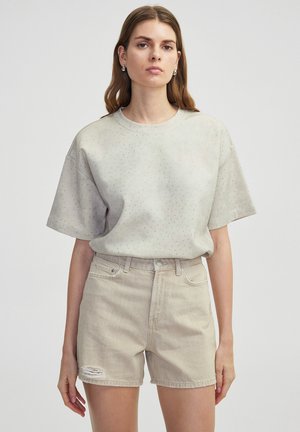 T-shirt gris clair à manches courtes avec de petits détails en motif, associé à un short en denim beige taille haute avec un ourlet effiloché.