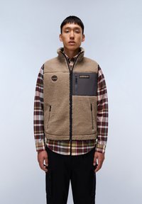 Fleece vest in tan with a high collar, zip pockets, and grey accent panel; worn over a checked shirt. Soft texture, casual design.
