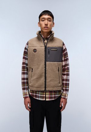 Fleece vest in tan with a high collar, zip pockets, and grey accent panel; worn over a checked shirt. Soft texture, casual design.