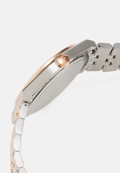 Round wristwatch with a stainless steel band and rose gold accents. Features a textured case and a prominent crown with an engraved logo.