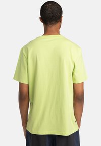 Lysegrøn bomulds-T-shirt med korte ærmer, rund hals og en ensfarvet rygdesign. Indeholder et lille mærke ved bundkanten.