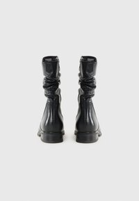 Svarta läderankelboots med samlad textur, rund tå och en låg staplad häl. Har elastiska sidopaneler och minimal sömnad.