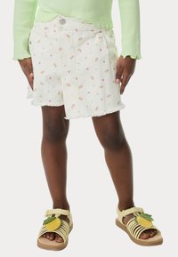 Pantalones cortos de mezclilla blanca con patrones florales coloridos, bordes deshilachados y bolsillos frontales, combinados con sandalias amarillas con un diseño de limón.