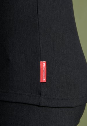 Top de tela negra con una costura lateral y una etiqueta roja. Textura suave con detalles de costura que enfatizan un diseño ajustado.