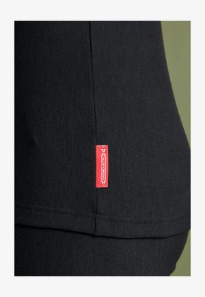 Haut en tissu noir avec une couture latérale et une étiquette rouge. Texture lisse avec des détails cousus, mettant en avant une coupe ajustée.