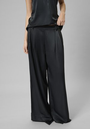 Schwarze weite Hosen aus einem glatten, glänzenden Stoff mit hoher Taille, Falten an der Vorderseite und einer entspannten Drapierung am Saum.