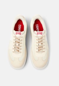 Beige Sneaker mit Netz- und Wildleder-Optik, ausgestattet mit beigen Schnürsenkeln, rotem Branding auf der Innensohle und der Zunge sowie einer Gummisohle.