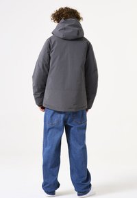 Chaqueta con capucha gris de corte relajado, con una textura suave. Se lleva con vaqueros azules holgados y zapatillas blancas, visto desde la parte de atrás.