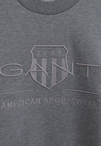 Grijze sweatshirt met gebreide ronde hals. Voorzien van een geborduurd schildlogo en "GANT" in zacht, lichtgrijs garen. Eenvoudige, gestructureerde stof.