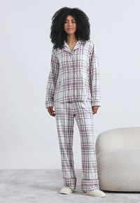 Conjunto de pijama de cuadros en algodón, con fondo blanco y líneas rojas y azul marino, mangas largas y pantalones de corte relajado.