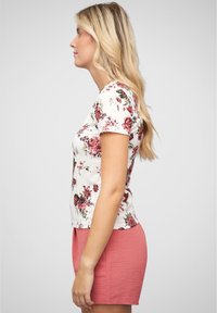 Haut à manches courtes floral blanc avec des motifs floraux roses et foncés, associé à un short texturé corail avec une poche latérale.