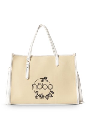 Beige canvas draagtas met witte leren accenten, voorzien van zwarte bloememborduring en logo in een cirkelontwerp, rechthoekige vorm en dubbele handvatten.