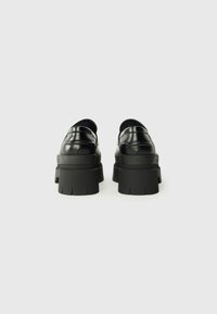 Black leather platform shoes with a rounded toe, featuring a thick, textured sole and subtle stitching details on the upper.