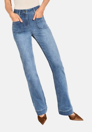 Person trägt hellblaue Straight-Leg-Jeans mit großen Fronttaschen und braune spitze Absätze mit Händen in den Taschen.