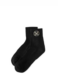 Calcetines de algodón negros con puños acanalados y un parche circular con logo en un lado. Textura suave, diseño hasta el tobillo, con zona del dedo reforzada.