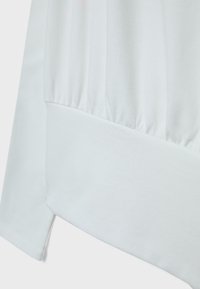 Zbliżenie na białą tkaninę z marszczonym szwem elastycznym i szerokim mankietem.