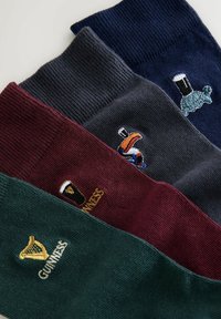 Set aus drei gestrickten Socken: dunkelgrün, burgunderrot und navy. Jede Socke hat einzigartig bestickte Designs, darunter eine Harfe und einen Tukan.