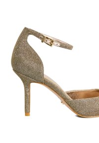 Gold sparkly high heel shoe with an ankle strap and a pointed toe design. The texture is shiny with a soft interior and a slender heel.