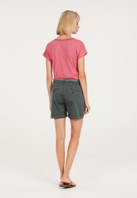 Camicia rosa a maniche corte con risvolti, abbinata a pantaloni corti verdi scuri con cintura e due tasche posteriori, mostrata da dietro.