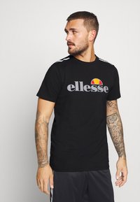 Black short-sleeve t-shirt with gray "ellesse" logo and colorful graphic, featuring white-striped shoulders and a smooth cotton texture.