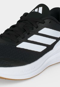 Ασπρόμαυρο αθλητικό παπούτσι Adidas με τρεις λευκές ρίγες, μαύρα κορδόνια και λευκή μαλακή σόλα με την επιγραφή "Cloudfoam."
