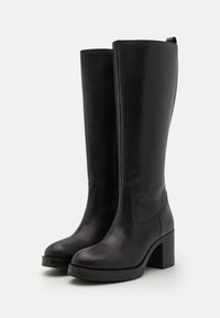 Bottes en cuir noir montant jusqu'aux genoux, avec un bout carré et un talon bloc. Texture lisse avec un léger éclat et une fermeture éclair latérale.